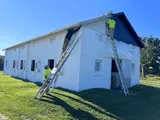 Professional painting contractors using tall extension ladders to paint a large white commercial building.